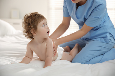 Photo of Orthopedist examining little baby on bed indoors