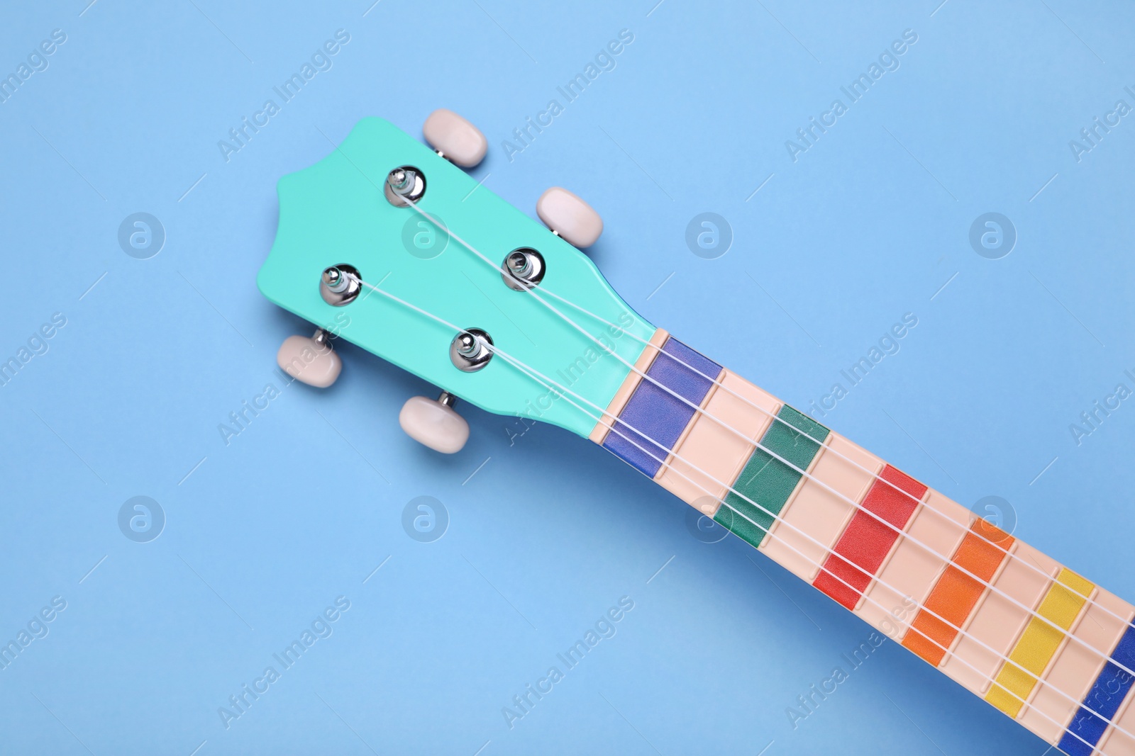 Photo of Colorful ukulele neck on light blue background, top view. String musical instrument