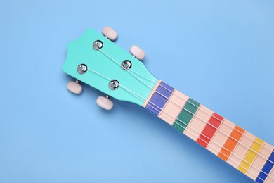 Colorful ukulele neck on light blue background, top view. String musical instrument