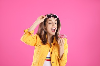 Beautiful young woman wearing sunglasses with donut on pink background