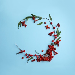 Photo of Red berries and leaves arranged in shape of wreath on light blue background, flat lay with space for text. Autumnal aesthetic