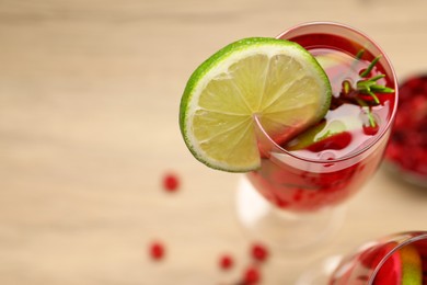 Photo of Tasty cranberry cocktail with rosemary and lime in glass on beige table, closeup. Space for text