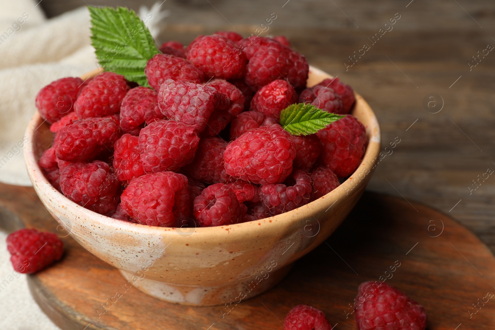 Photo of Bowl with delicious ripe raspberries on cutting board, closeup