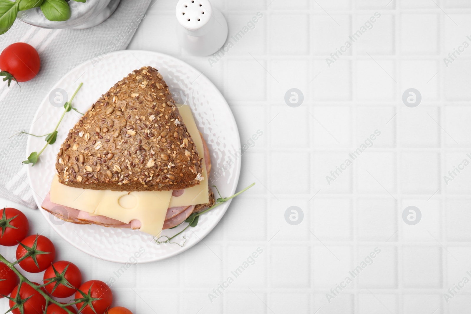 Photo of Delicious sandwich with ham, cheese and tomatoes on white tiled table, flat lay. Space for text