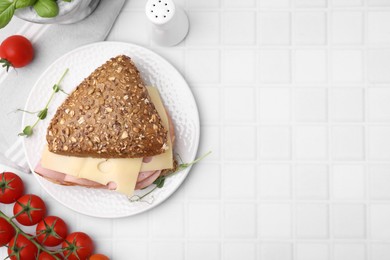 Delicious sandwich with ham, cheese and tomatoes on white tiled table, flat lay. Space for text