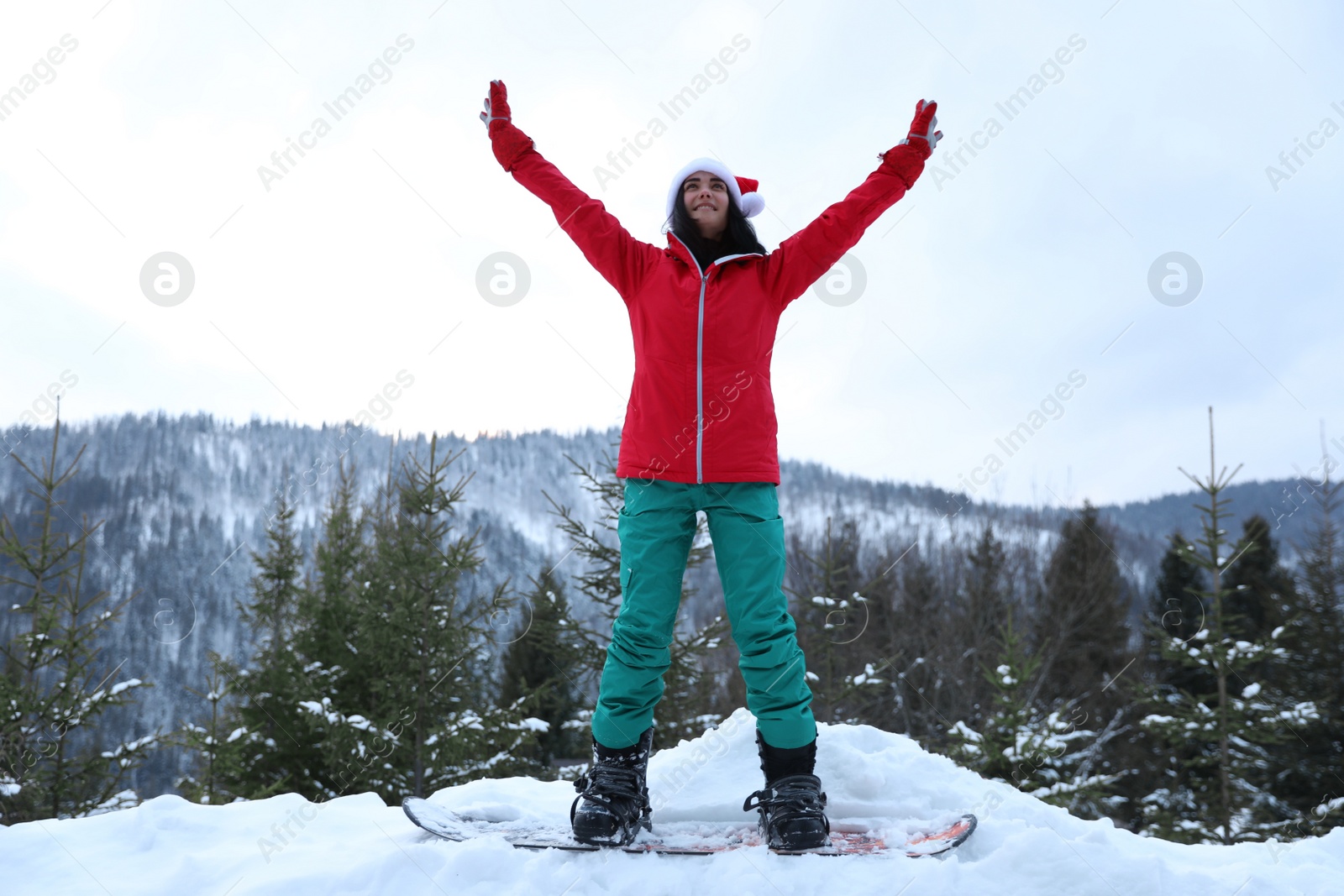 Photo of Young snowboarder wearing Santa hat on snowy hill. Winter vacation