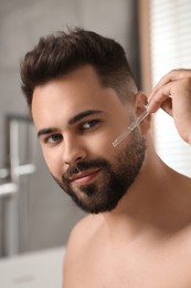 Photo of Handsome man applying cosmetic serum onto his face in bathroom