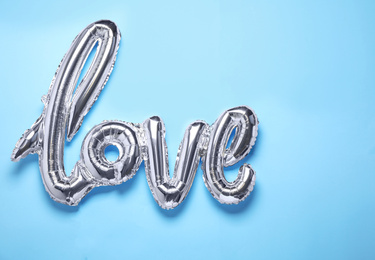 Photo of Foil LOVE word balloon on light blue background, top view
