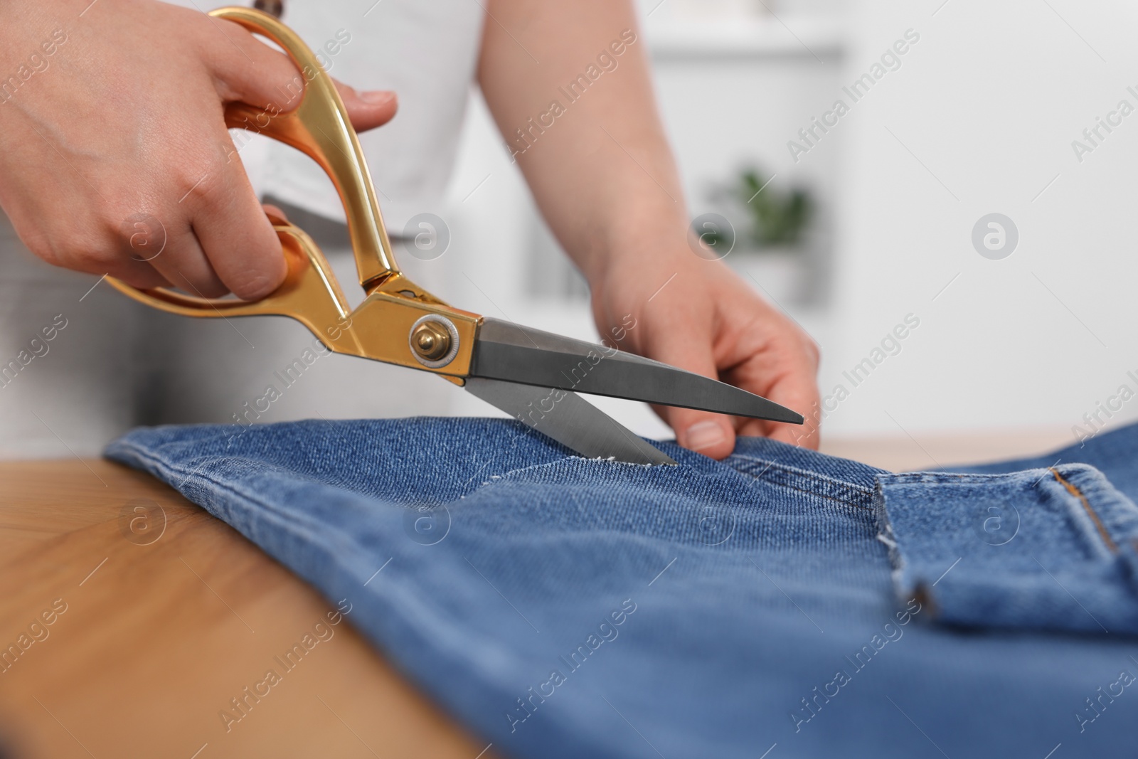 Photo of Woman making ripped jeans at wooden table, closeup