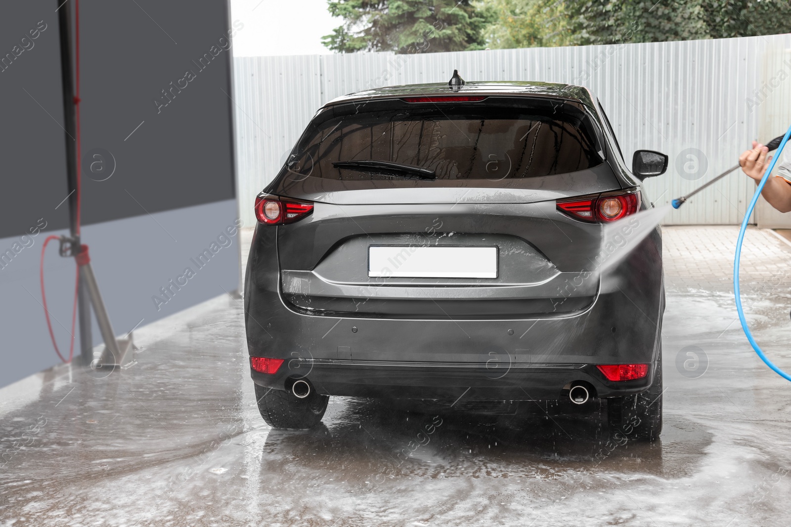 Photo of Man washing auto with high pressure water jet at car wash, closeup