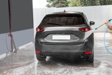 Man washing auto with high pressure water jet at car wash, closeup