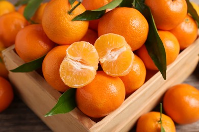 Photo of Delicious tangerines with leaves in crate on table, above view