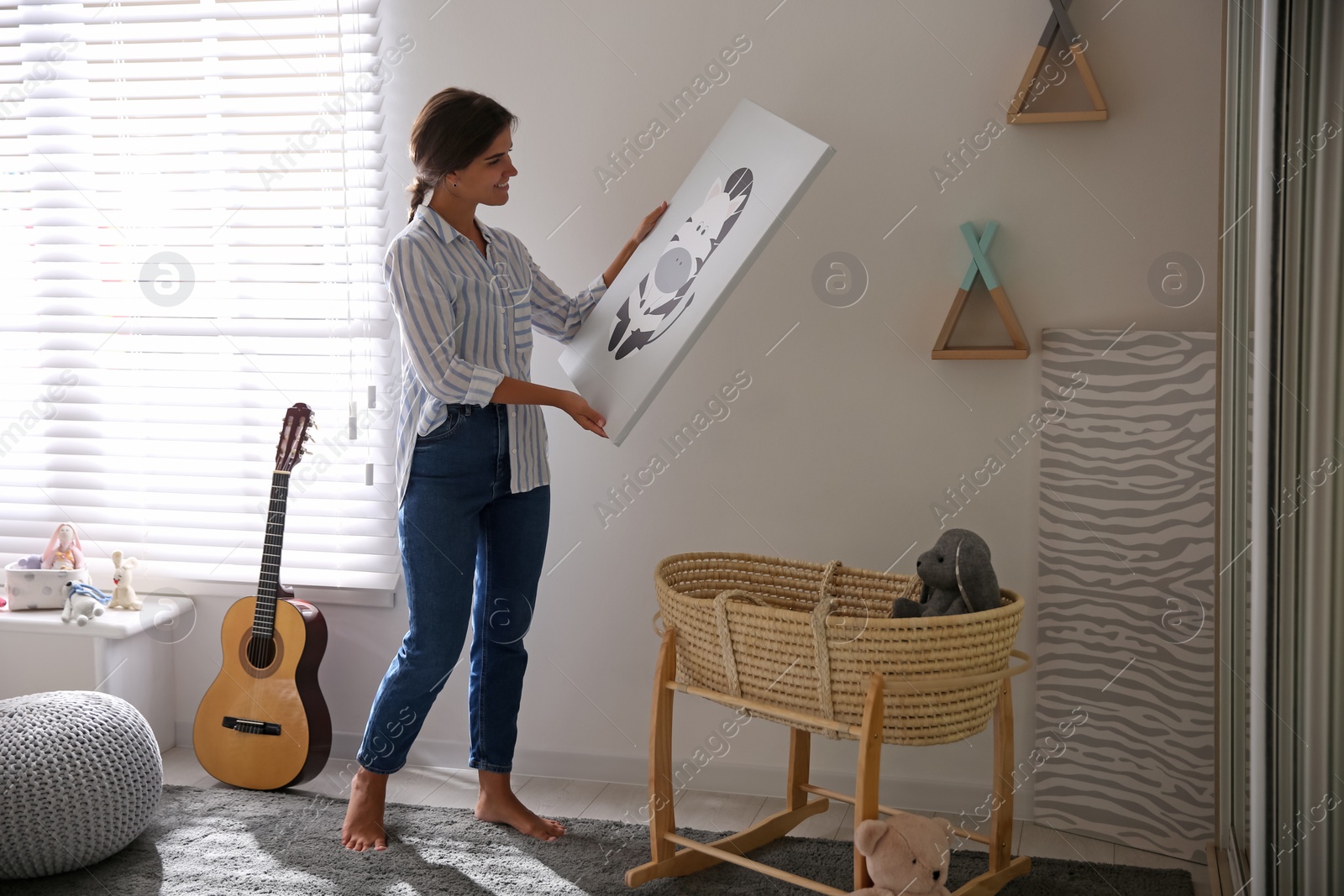 Photo of Decorator hanging picture on white wall in baby room. Interior design