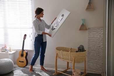 Decorator hanging picture on white wall in baby room. Interior design