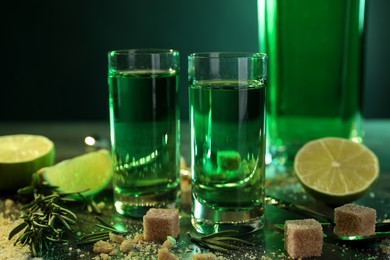 Photo of Absinthe in shot glasses, brown sugar, lime and rosemary on table, closeup. Alcoholic drink
