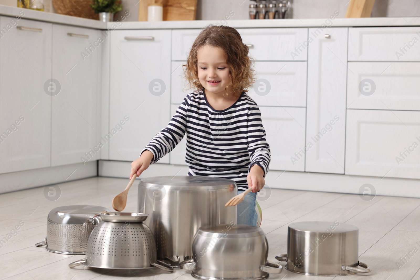 Photo of Little girl pretending to play drums on pots in kitchen