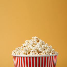 Photo of Delicious popcorn in paper bucket on yellow background, closeup