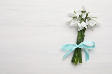 Photo of Beautiful snowdrop flowers with ribbon on white wooden table, top view. Space for text