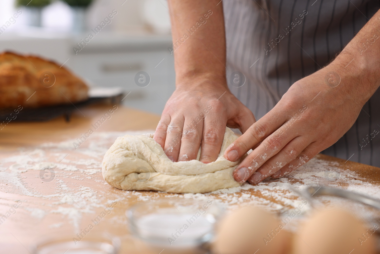 Photo of Making bread. Man kneading dough at wooden table in kitchen, closeup