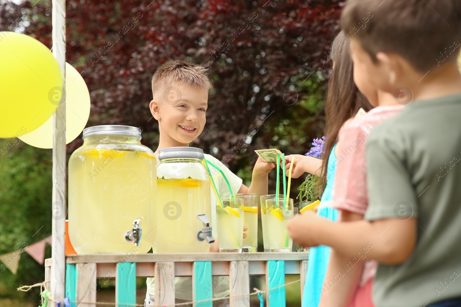 Photo of Little boy selling natural lemonade at stand in park