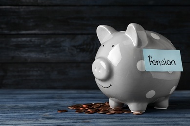 Photo of Piggy bank with word PENSION and coins on table. Space for text