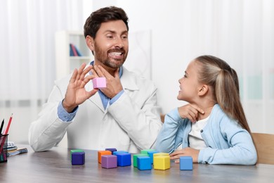 Photo of Dyslexia treatment. Speech therapist holding cube while working with girl at table in room
