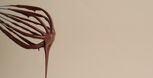 Image of Whisk with yummy chocolate cream on color background, closeup. Banner design with space for text