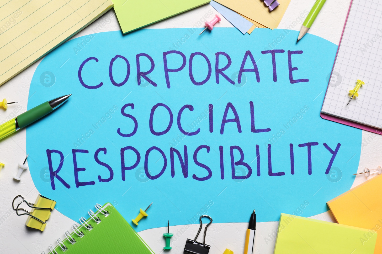 Photo of Paper text balloon with phrase Corporate Social Responsibility among office supplies on white table, flat lay