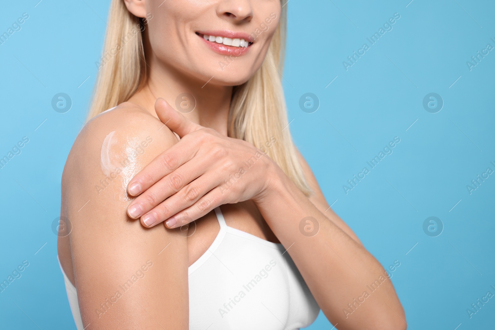 Photo of Woman applying body cream onto her arm against light blue background, closeup. Space for text