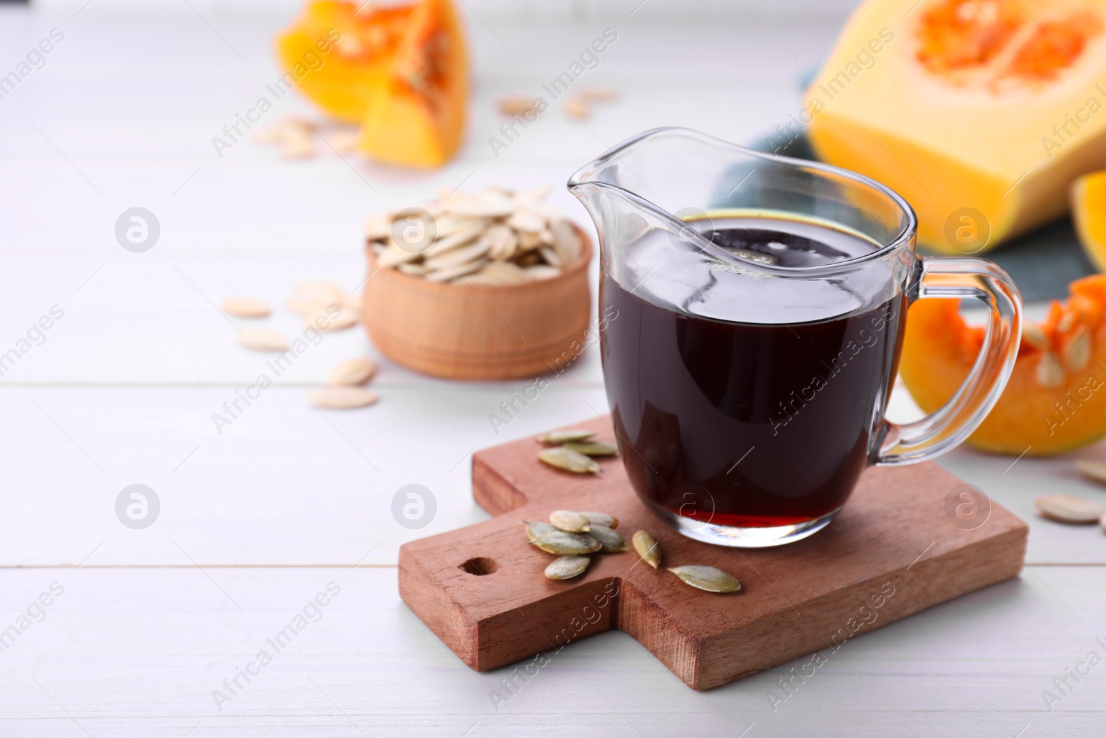 Photo of Fresh pumpkin seed oil in glass pitcher on white wooden table. Space for text