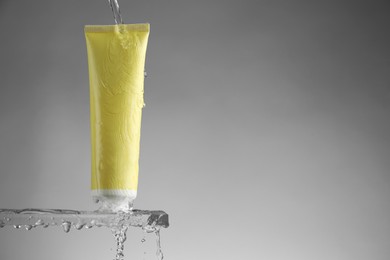 Photo of Moisturizing cream in tube on glass with water drops against grey background. Space for text