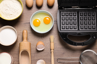 Flat lay composition with ingredients and Belgian waffle maker on wooden table