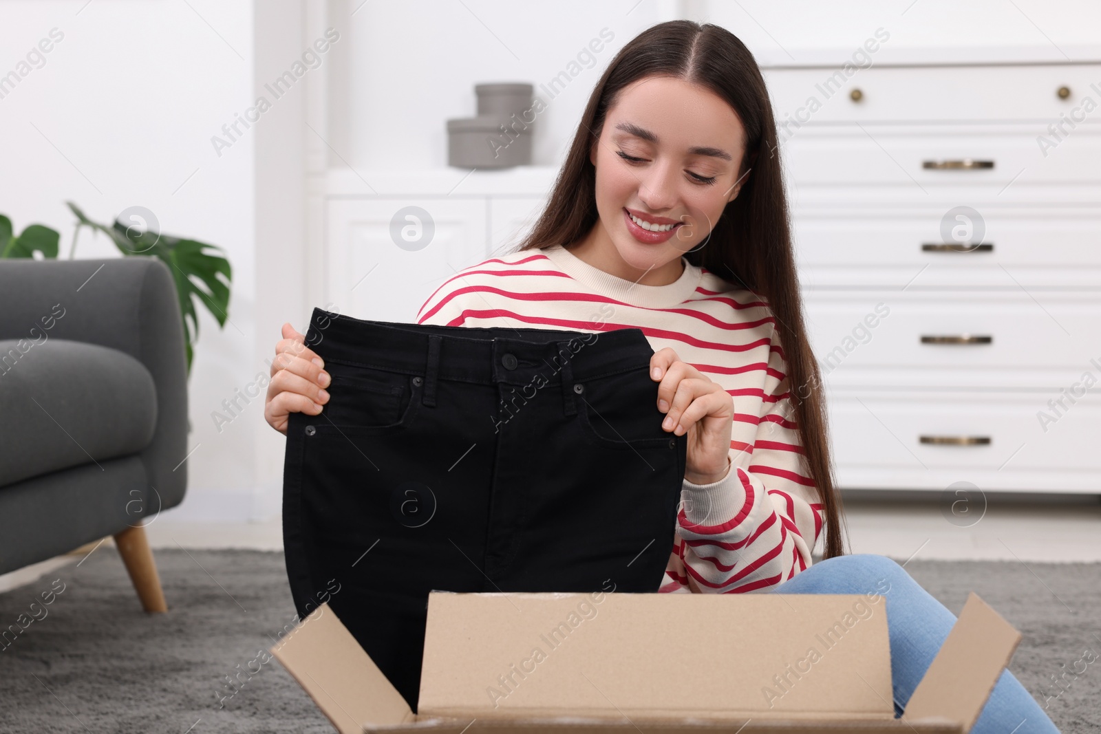 Photo of Happy young woman taking black jeans out of box at home. Online shopping