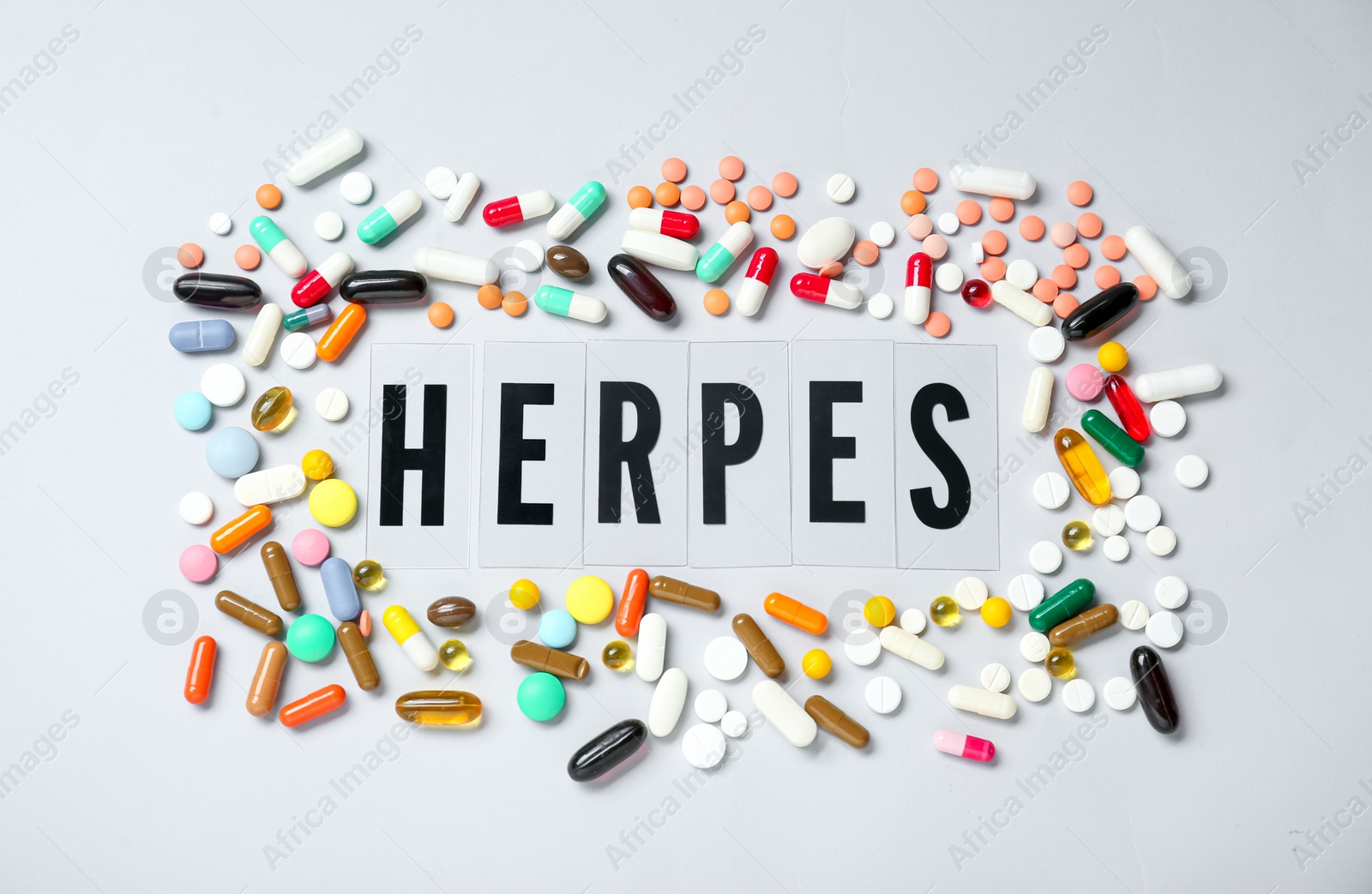 Photo of Word Herpes surrounded by different pills on white background, top view