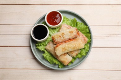 Photo of Delicious fried spring rolls and sauces on light wooden table, top view