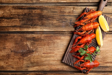 Photo of Board with delicious boiled crayfishes on wooden table, top view. Space for text