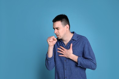 Photo of Young man coughing on blue background, space for text. Cold symptoms