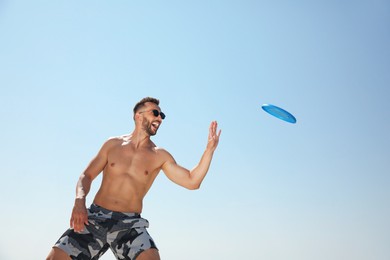 Happy man catching flying disk against blue sky on sunny day