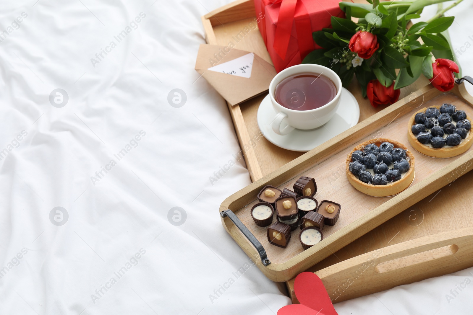 Photo of Tasty breakfast served in bed. Delicious desserts, tea, flowers and gift box on tray, space for text