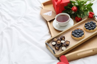 Photo of Tasty breakfast served in bed. Delicious desserts, tea, flowers and gift box on tray, space for text