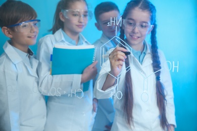 Pupils writing chemistry formula on glass board against color background