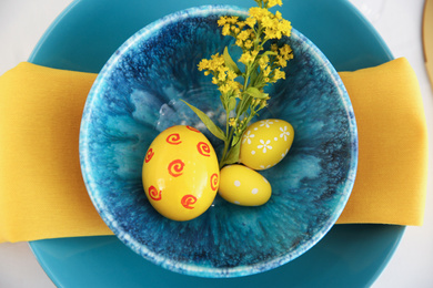 Photo of Easter eggs and mimosa flower in bowl on white background, top view. Festive table setting