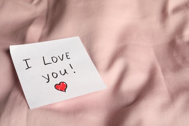 Photo of Sticky note with phrase I love you! on bed, closeup. Space for text