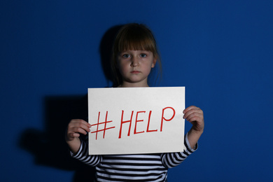 Abused little girl with hashtag HELP near blue wall. Domestic violence concept