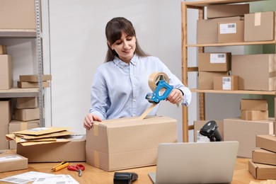 Photo of Parcel packing. Post office worker taping box at wooden table indoors