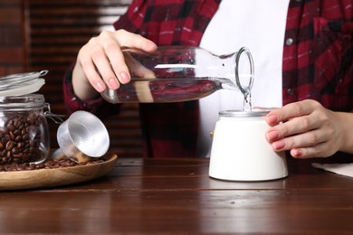 Photo of Brewing coffee. Woman pouring water into moka pot at wooden table indoors, closeup