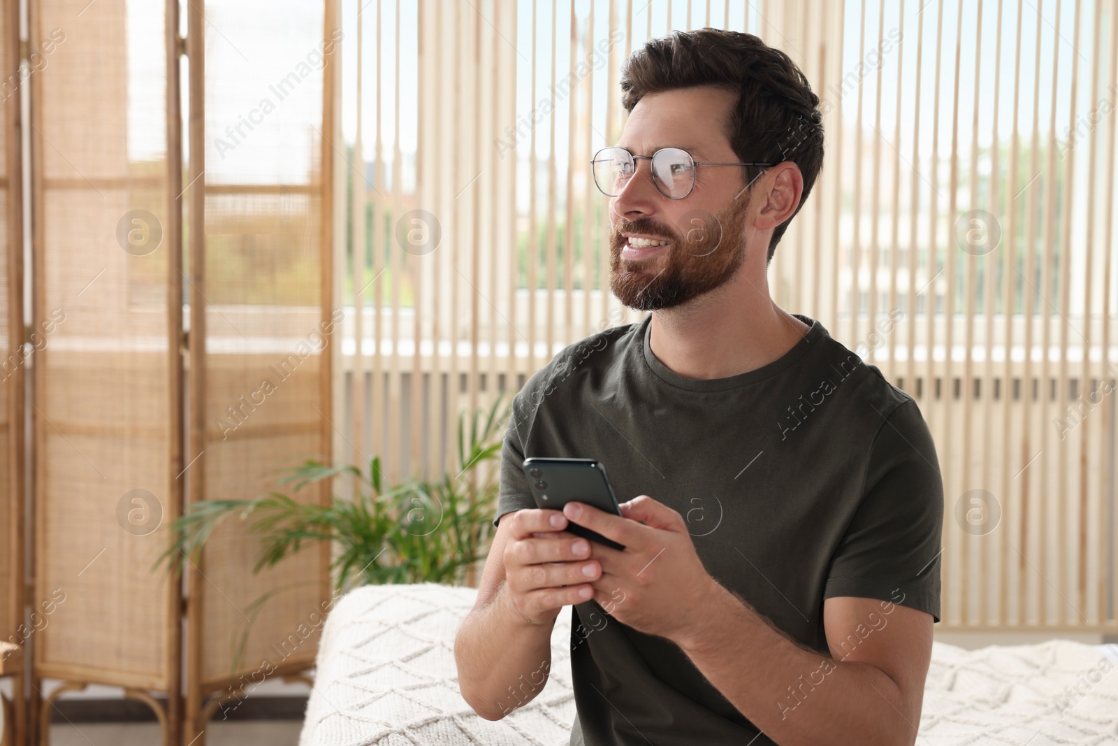 Photo of Handsome man using smartphone at home, space for text
