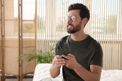 Handsome man using smartphone at home, space for text