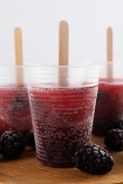 Photo of Tasty blackberry ice pops in plastic cups on table, closeup. Fruit popsicle
