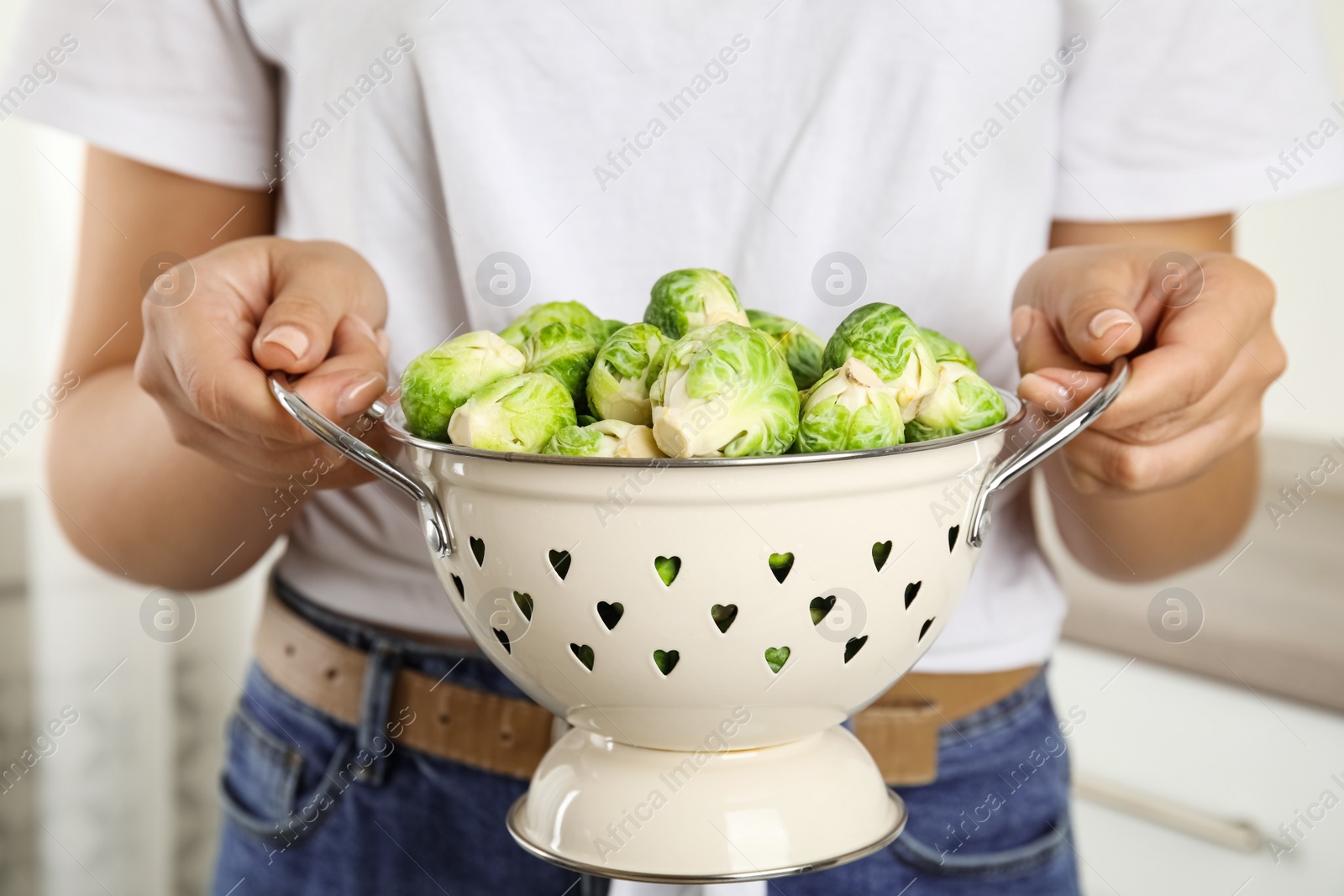 Photo of Woman holding colander with Brussels sprouts on blurred background, closeup